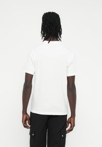 Baltas trumpomis rankovėmis medvilninis marškinėlis su apvalia iškirpte ir laisvu siluetu, derinamas su juodomis kargo kelnėmis.