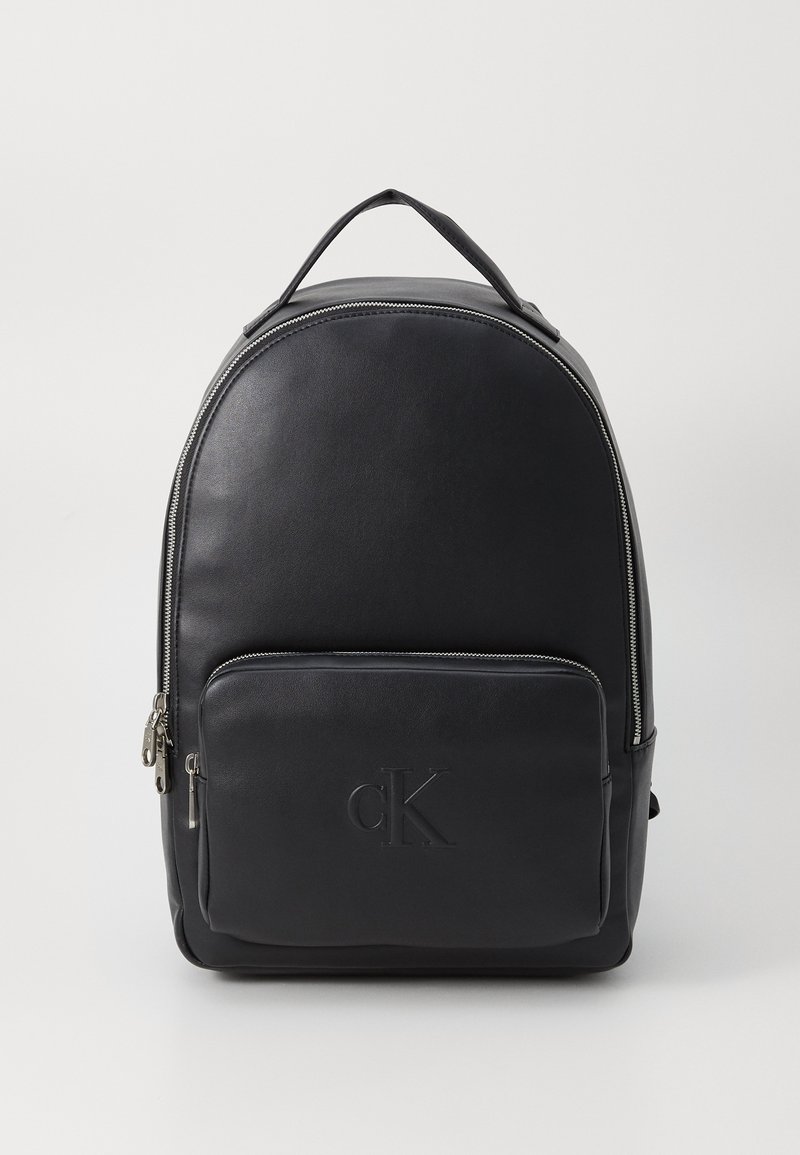 Black leather backpack with rounded shape, silver zipper, front pocket, embossed logo, and top handle for carrying.