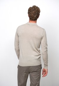 Suéter beige claro con tejido texturizado, mangas largas y dobladillo acanalado. La parte trasera presenta un diseño sencillo sin logotipos ni patrones visibles.