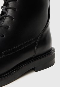 Black leather boot with laces, detailed stitching along the side, and a thick sole on a white background.