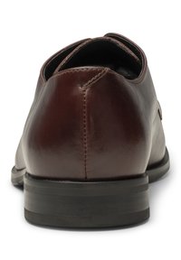 Chaussure habillée pour homme en cuir marron foncé vue de dos, montrant les coutures, surface lisse et semelle noire avec un talon bas.
