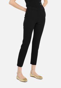 Schwarze maßgeschneiderte Hose mit schlankem Schnitt, flachem Vorderteil und seitlichen Taschen, kombiniert mit goldenen Ballettschuhen mit dekorativem Akzent.