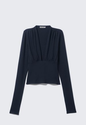 Tumši zils garām piedurknēm krekls ar dziļu V-veida kaklu, savilktām plecu daļām un piegulošu korpusu ar nedaudz izvērstu apakšu. Izgatavots no mīksta auduma.