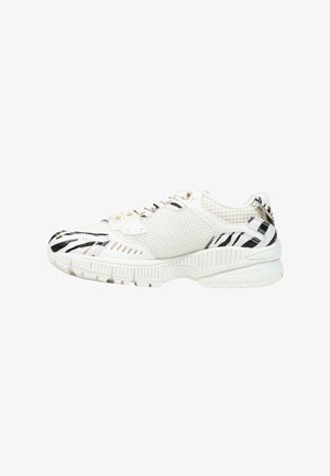 Zapatilla blanca con paneles de malla y rayas negras de cebra en la puntera, el talón y los detalles superiores, con suela gruesa y cierre de cordones.