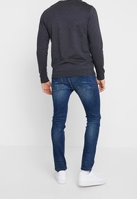 Ciemnoszara, długosługa koszula w połączeniu z niebieskimi, obcisłymi dżinsami. Stylizacja jest uzupełniona białymi trampkami i charakteryzuje się prostym, casualowym designem.