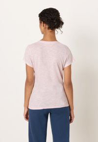 Svetlo rožnata majica s kratkimi rokavi in okroglim izrezom. Mehka, rahlo teksturirana tkanina. Šivi na ramenih. Kombinirana z mornarsko modrimi hlačami.