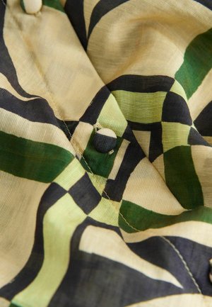 Tkanina wzorzysta w czarne, zielone i kremowe pasy, z okrągłym guzikiem i miękkim, teksturowanym wykończeniem.