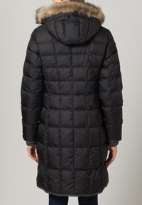 Zwarte donsjas met een capuchon, voorzien van een nepbontafwerking. Gequilte designe en geribbelde manchetten zorgen voor extra warmte en textuur.