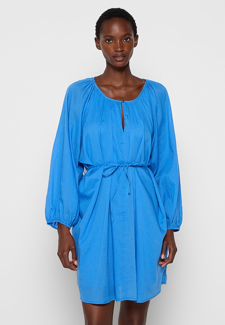 Vestido azul, hasta la rodilla, hecho de una tela ligera, con cuello redondo, mangas largas abullonadas, un detalle de ojal y una cintura ajustada con lazo.