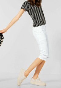 Černobílý pruhovaný krátký rukáv košile spárovaný s bílými capri kalhotami a béžovými teniskami, s hladkou texturou a ležérním designem.