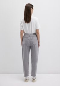 Graue hochtaillierte Hose mit strukturierter Oberfläche, ausgestattet mit einem Design von Gesäßtaschen und kombiniert mit einem schlichten weißen T-Shirt und Sneakers.