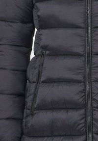 Veste en duvet noire avec un design matelassé horizontal, dotée d'une poche zippée et d'une texture lisse. Matériau léger et isolant.