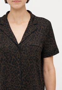 Kratka pidžama košulja s kratkim rukavima u tamnosmeđoj boji s crnim leopardskim uzorkom, s detaljima poput ovratnika i džepa na lijevoj strani. Vidljivi gumbi.