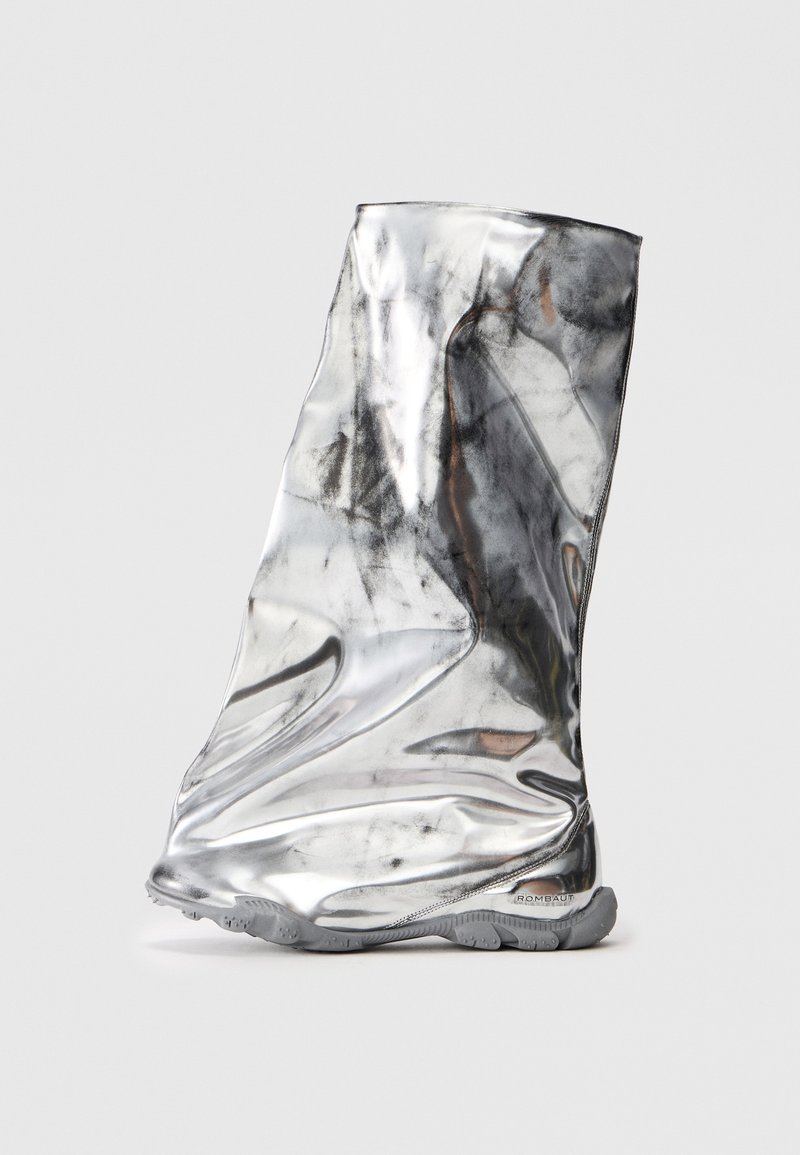 Botín plateado hecho de un material reflectante con una textura suave y arrugada. Cuenta con una construcción flexible y suela de goma gris.