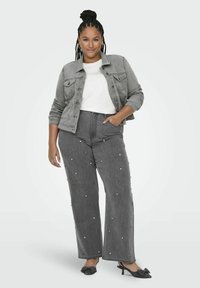 Pilka džinsinė striukė ant baltos marškinėlių, derinama su pilkomis plačiomis kelnių, puoštomis pasklidomis baltomis detalėmis, ir juodais bateliais su kaspinu.