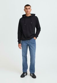 Hanorac negru cu glugă și sireturi, asortat cu blugi bleumarin deschis și adidași negri cu dungi albe. Design simplu, croială lejeră.