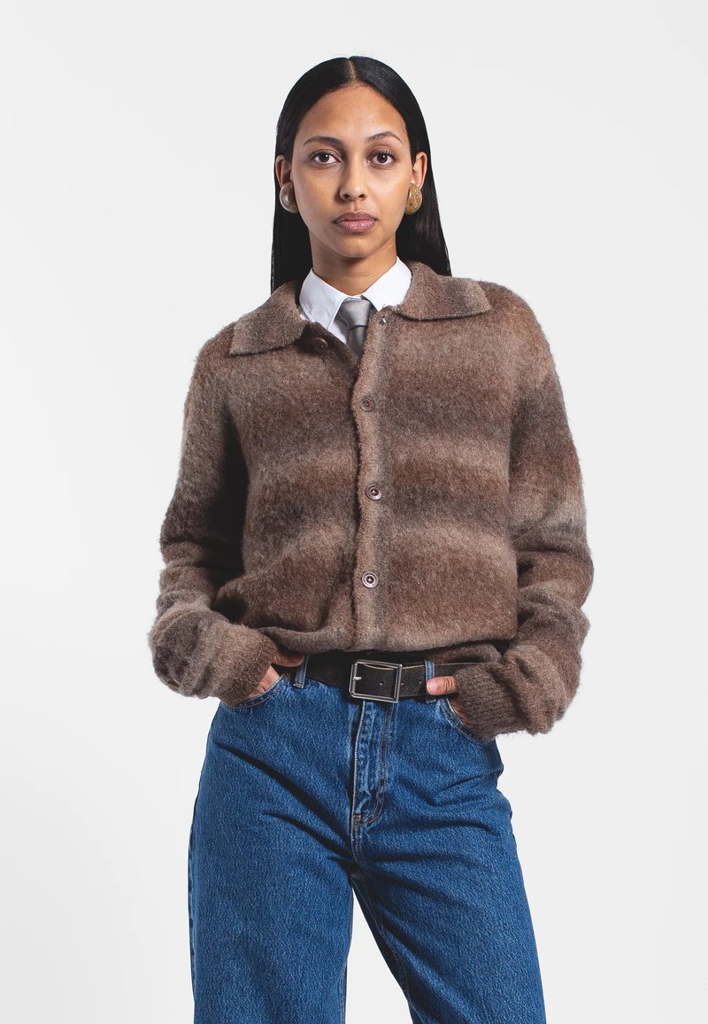 Cardigan marron et duveteux avec un col, quatre boutons et des manches longues, accompagné d'un jean bleu taille haute et d'une chemise blanche à col.