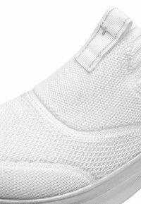 Baskets blanches à enfiler avec une tige en tricot texturé, bande élastique à l'ouverture et semelle en caoutchouc lisse. Présente des éléments de design minimalistes.