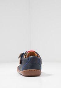 Scarpa in pelle blu con suola in gomma marrone. Vista posteriore che evidenzia accenti contrastanti in marrone e arancione, forma arrotondata e dettagli cuciti.