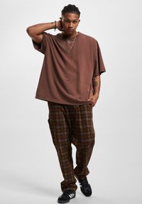 Brown oversized T-shirt with rolled sleeves, paired with plaid baggy trousers in earthy tones. Black sneakers complete the outfit.