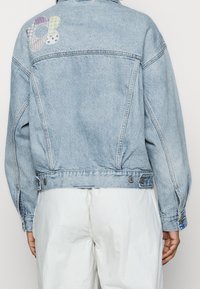 Giacca di jeans blu chiaro con una vestibilità rilassata, caratterizzata da un patch multicolore di tessuti a righe e a pois sulla parte superiore della schiena.