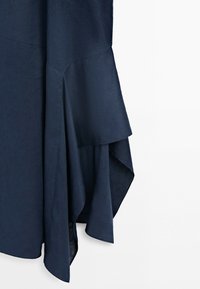 Tissu bleu foncé avec un ourlet évasé et asymétrique créant des plis superposés et fluides sur un fond clair uni.