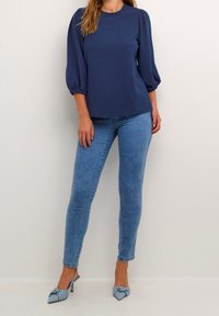 Top blu navy con texture e maniche a sbuffo abbinato a jeans skinny azzurri e tacchi appuntiti blu con dettaglio a fiocco.