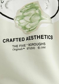 Tela blanca con texto negro que dice "CRAFTED AESTHETICS THE FIVE * BOROUGHS Originals™ STUDIO © 1990," acompañado de una ilustración de alcachofa verde.