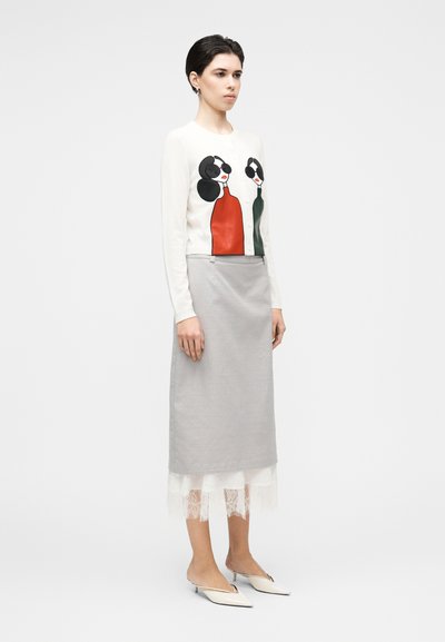 Pleteni pulover z grafičnim dizajnom, ki prikazuje dve postavi v rdeči in zeleni barvi, kombiniran z sivim svinčnikom krilo z čipkasto obrobo, dopolnjen z belimi čevlji.