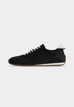 Czarny niski sneaker z białymi sznurowadłami, białą zakładką na pięcie i brązową gumową podeszwą na prostym jasnym tle.