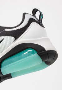 Sneaker med en vit och svart ovandel, mesh- och syntetmaterial, med en synlig turkos luftkudde i sulan.