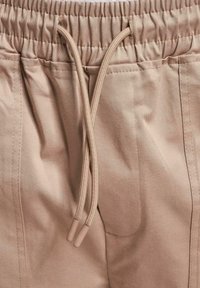 Beige narashoushoushikura pants la'e an elastic waistband, textured fabric, ekja side pockets. Anno a narashoushoushikura ani plastic tips e le ishi shiyou.