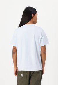 T-shirt en coton bleu clair à manches courtes, avec un col rond et un ourlet droit, porté avec un pantalon vert olive. Pas de motifs visibles.