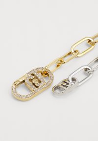Gull- og sølvkjede-armbånd med en gyllen hengelås prydet med edelstener; slankt design med alternerende lenketyper.
