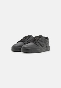 Black leather sneakers featuring a textured surface, lace-up closure, and a flat rubber sole with traction patterns. Notable "N" logo on the side.
