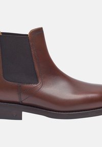 Bottine en cuir marron avec des panneaux latéraux élastiques, texture lisse, bout rond et un petit talon empilé. Présente une couture contrastante.