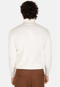 Maglione bianco a maglia con collo alto, caratterizzato da un motivo testurizzato e polsini a costine, indossato con pantaloni marroni. Vista posteriore mostrata.