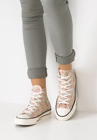 Hoge sneakers met een meerkleurig, gepatterned canvas bovenwerk, witte veters en een zwarte rubberen zool. G gedragen bij omgeslagen grijze broeken.