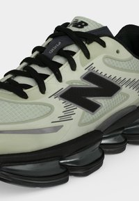 Крупен план на бежово и черно бягащо обувка New Balance с черни връзки и сегментирана омекотена подметка.