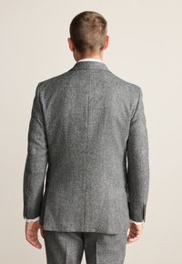 Veste de costume en tweed gris vue de dos, présentant un design structuré, une texture subtile et des revers crantés. Boutons visibles sur les manches.
