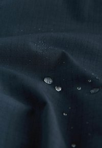 Tissu sombre à motif quadrillé montrant des gouttes d'eau perlant à sa surface, démontrant des propriétés déperlantes.