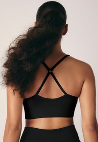 Zwarte geribbelde sport-bh met een cross-back ontwerp en dunne bandjes, benadrukt een gladde textuur en een strakke pasvorm.
