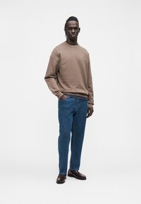 Καφέ φούτερ με στρογγυλή λαιμόκοψη, μπλε τζιν και καφέ μοκασίνια. Casual εφαρμογή και μονόχρωμα χρώματα, χωρίς εμφανή σχέδια ή λογότυπα.