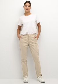 Beige cotton chinos with front pockets, paired with a plain white crew-neck t-shirt. Worn with white athletic shoes.