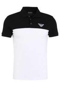 Svart och vit pikétröja med krage, tre knappar och en diskret logotyp på vänster bröst. Tillverkad i textilerad tyg.