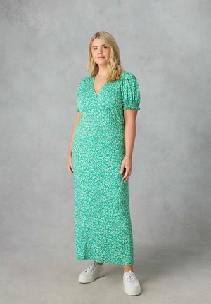 Robe maxi florale verte avec un décolleté en V, des manches bouffantes et une taille cintrée. Associée à des baskets blanches pour un look décontracté.
