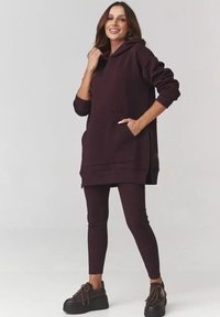 Winiakowy, bawełniany sweatshirt z kapturem, długimi rękawami, kieszenią z przodu i bocznymi rozcięciami, zestawiony z dopasowanymi legginsami i czarnymi sneakersami na platformie.