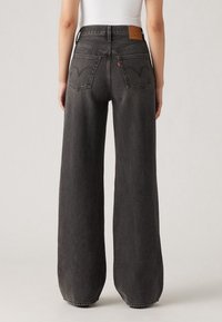 Černé džínové kalhoty s vysokým pasem a širokými nohavicemi, vyrobené z denimu, s klasickým designem pěti kapes a zadní nášivkou s logem, s hladkou texturou.