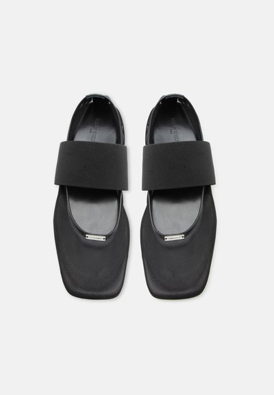 Ζευγάρι μαύρα παπούτσια με τετράγωνη μύτη, φαρδιές ελαστικές λωρίδες στο επάνω μέρος και υφασμάτινα επάνω μέρη με υφή, σε θέα από πάνω σε λευκό φόντο.