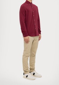 Camisa de manga larga burdeos con botones, pantalones chinos color beige y zapatillas blancas con detalles en negro. Diseño sencillo, corte ajustado y material de algodón.
